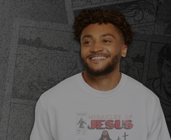 Smiling man in a Miracles of Jesus comic-cover sweatshirt in front of a wall of comic panels